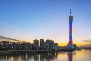 A cityscape with a prominent tower reflecting on the water, surrounded by high-rise buildings. - Yufei Smart City View Residence (Guangzhou)