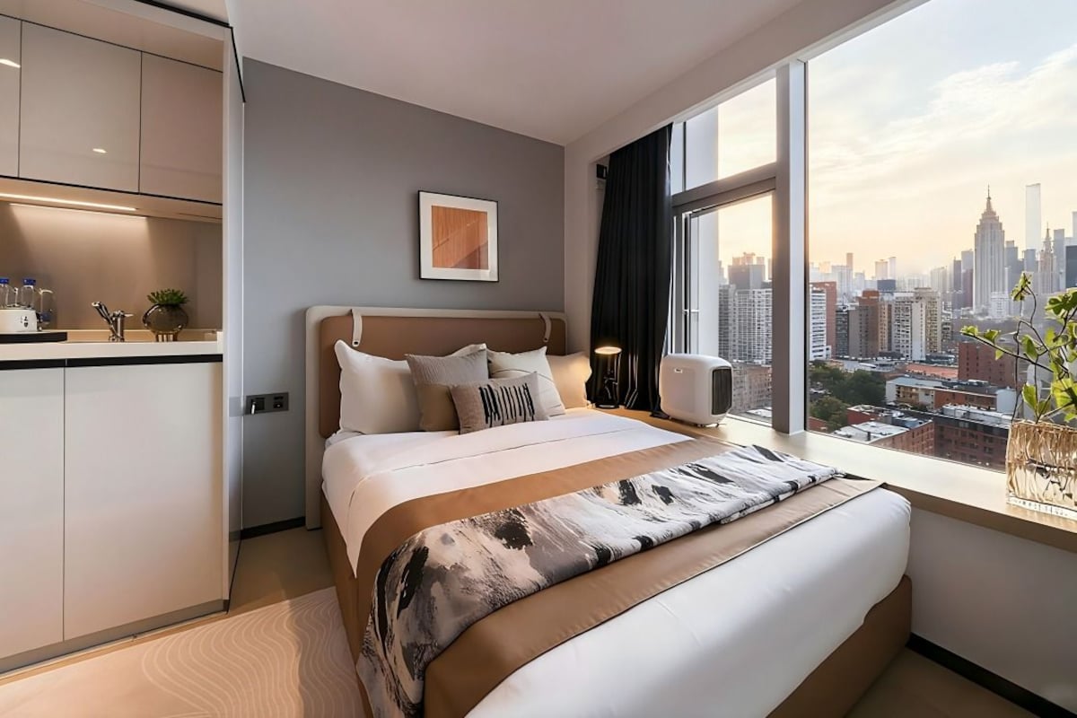 Una camera d'albergo moderna con un letto grande, vista sulla città, angolo cottura e un'ampia finestra.