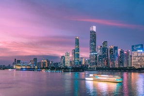 A city skyline at dusk with illuminated buildings reflecting on the water. - Yufei Smart City View Residence (Guangzhou)