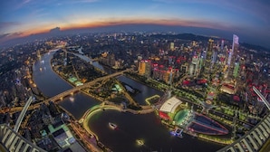Una vista panorámica de un paisaje urbano al atardecer con edificios iluminados, un río y un puente.