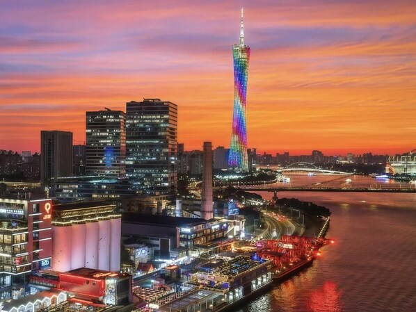 A cityscape at dusk with a prominent tower illuminated in the center, surrounded by modern buildings and a river. - Yufei Smart City View Residence (Guangzhou)