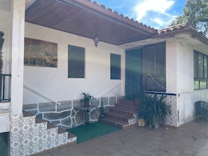 Un edificio con fachada de tejas, una escalera que lleva a un acceso cubierto y plantas en macetas.