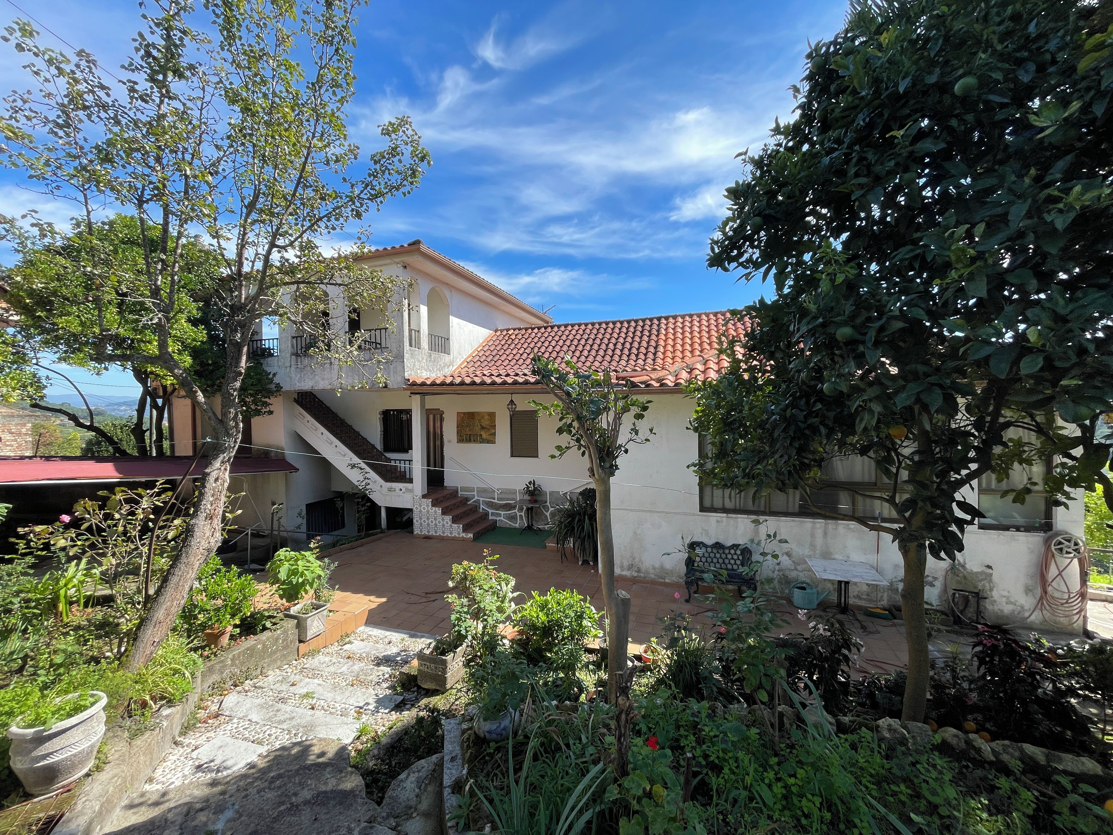 A two-story house with a tiled roof, a staircase, and a garden with various plants and a small pond.