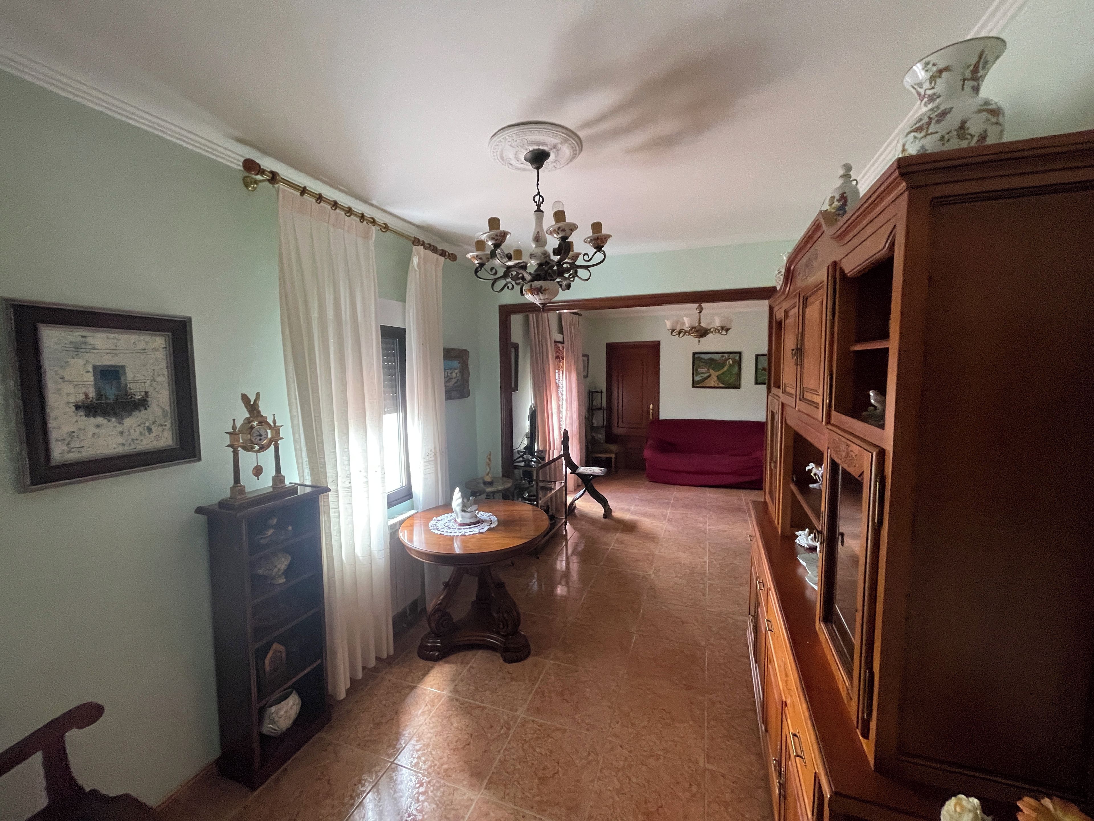 A spacious living room with a chandelier, a red sofa, and a wooden cabinet.