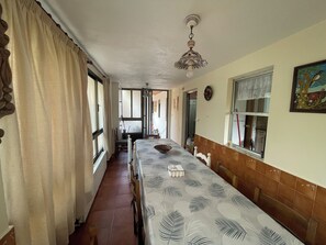 Un comedor con una mesa larga, sillas, un ventilador de techo y una ventana con cortinas.