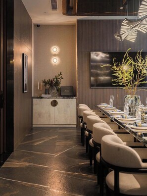 A modern dining area with a long table set for a meal, a decorative wall with a flat-screen TV, and a minimalist decor style. - The Nelson Luxury 3BR Apartment in Lang Ha street – Free Pool, Gym & Sauna (Hà Nội)