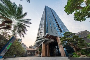 A modern high-rise building with a glass facade, surrounded by lush greenery and palm trees. - The Nelson Luxury 3BR Apartment in Lang Ha street – Free Pool, Gym & Sauna (Hà Nội)