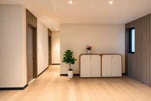 A hallway with wooden flooring, a potted plant, a white cabinet, and a window. - The Nelson Luxury 3BR Apartment in Lang Ha street – Free Pool, Gym & Sauna (Hà Nội)