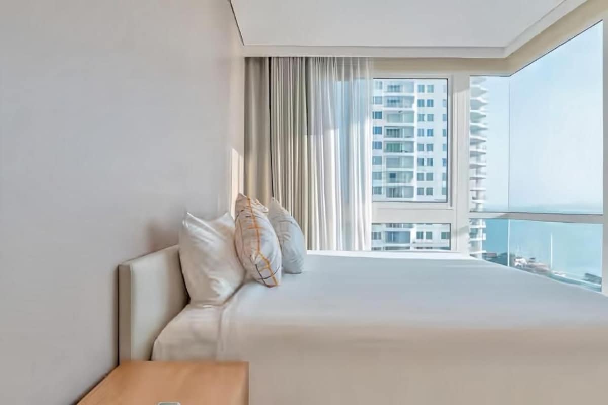 Une chambre d’hôtel avec un grand lit, une vue sur un immeuble de grande hauteur et une fenêtre avec des rideaux.