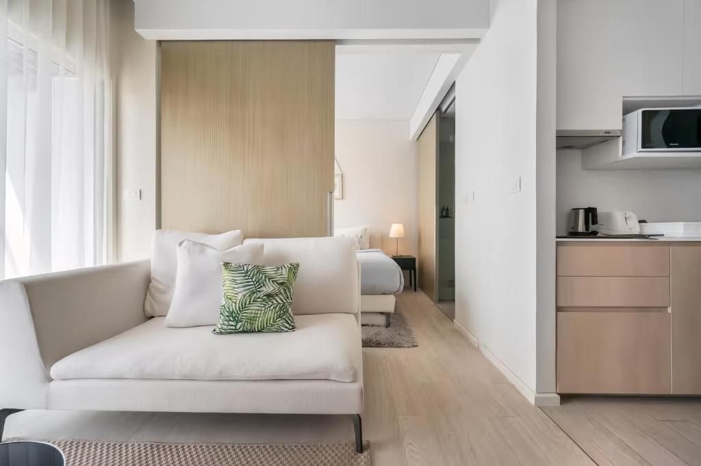 A modern hotel room with a sofa, a bed, a kitchenette, and a view of the hallway.