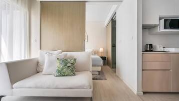 A modern hotel room with a sofa, a bed, a kitchenette, and a view of the hallway.