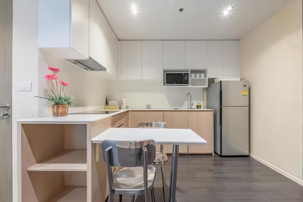 A modern kitchen with white cabinetry, a microwave, a refrigerator, and a dining area with a table and chairs.