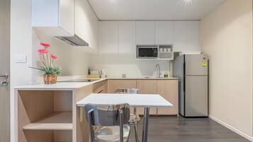 A modern kitchen with white cabinetry, a microwave, a refrigerator, and a dining area with a table and chairs.