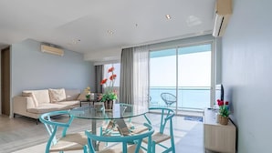Ein modernes Wohnzimmer mit Glastisch und Stühlen, einer Couch, einem Balkon mit Aussicht und einem kleinen Beistelltisch mit Pflanzen.
