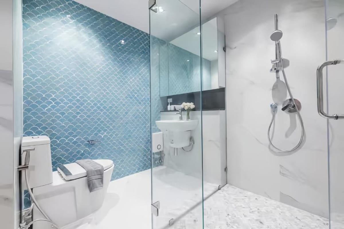 Une salle de bain moderne avec une douche à parois de verre, des toilettes blanches et un lavabo avec un pare-éclaboussures bleu en carrelage.