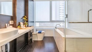 Ein modernes Badezimmer mit einer großen Badewanne, einer Toilette und einem Waschbecken. Ein Fenster sorgt für natürliches Licht und bietet einen Ausblick ins Freie.