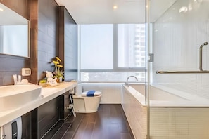 Une salle de bain moderne avec une grande baignoire, des toilettes et un lavabo. Une fenêtre laisse entrer la lumière naturelle et offre une vue sur l’extérieur.