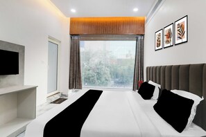 Ein modernes Hotelzimmer mit einem großen Bett, einem Flachbildfernseher, einem Fenster mit Vorhängen und gerahmten Bildern an der Wand.