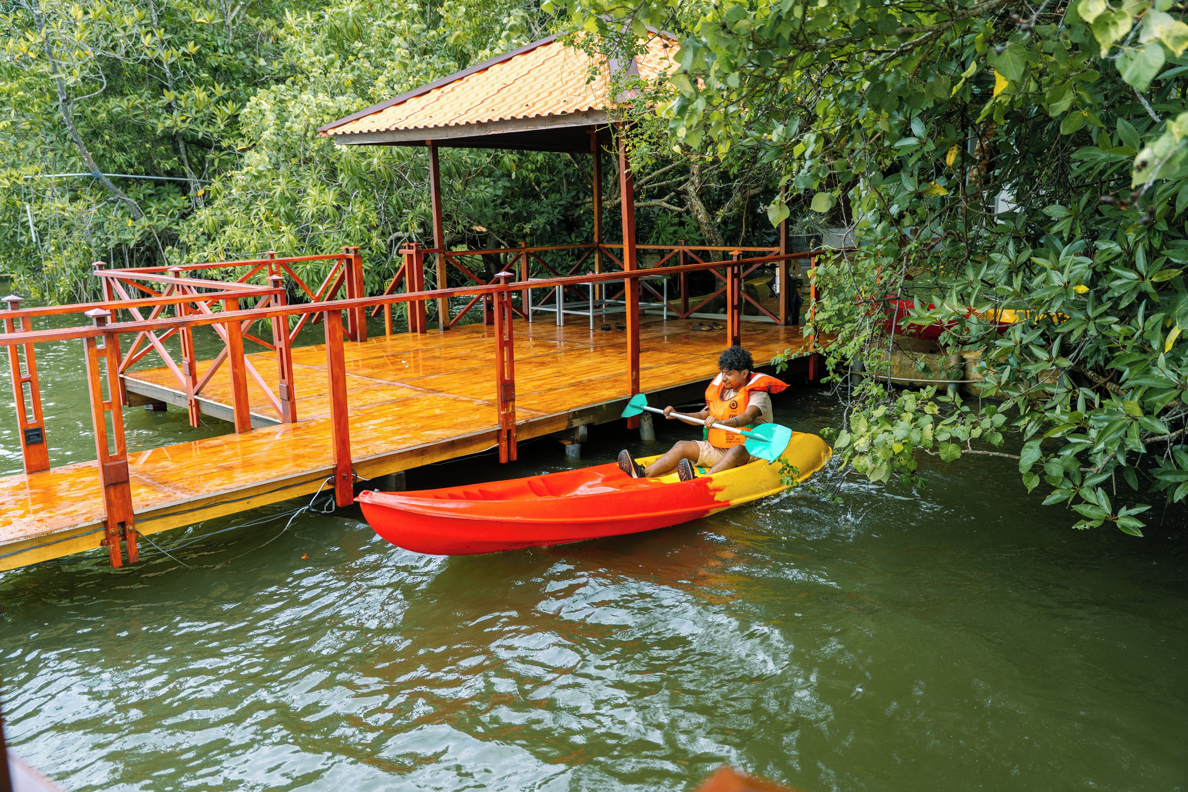 Une jetée en bois s’étendant dans une étendue d’eau, avec une petite embarcation et une personne portant un gilet de sauvetage jaune.