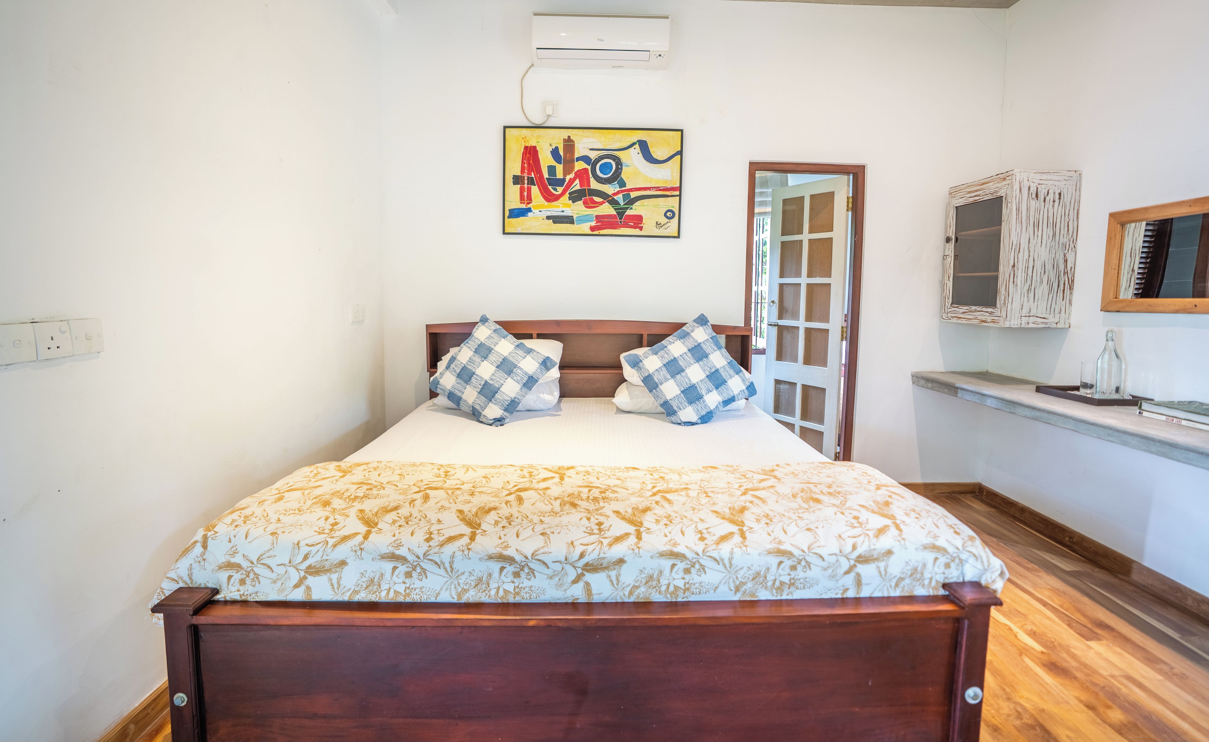A bed with a floral bedspread, a painting above it, and a wooden headboard.