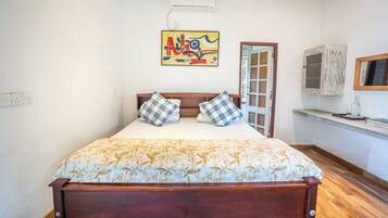 A bed with a floral bedspread, a painting above it, and a wooden headboard.