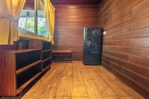 A compact kitchen with wooden walls, a refrigerator, and a window with curtains.