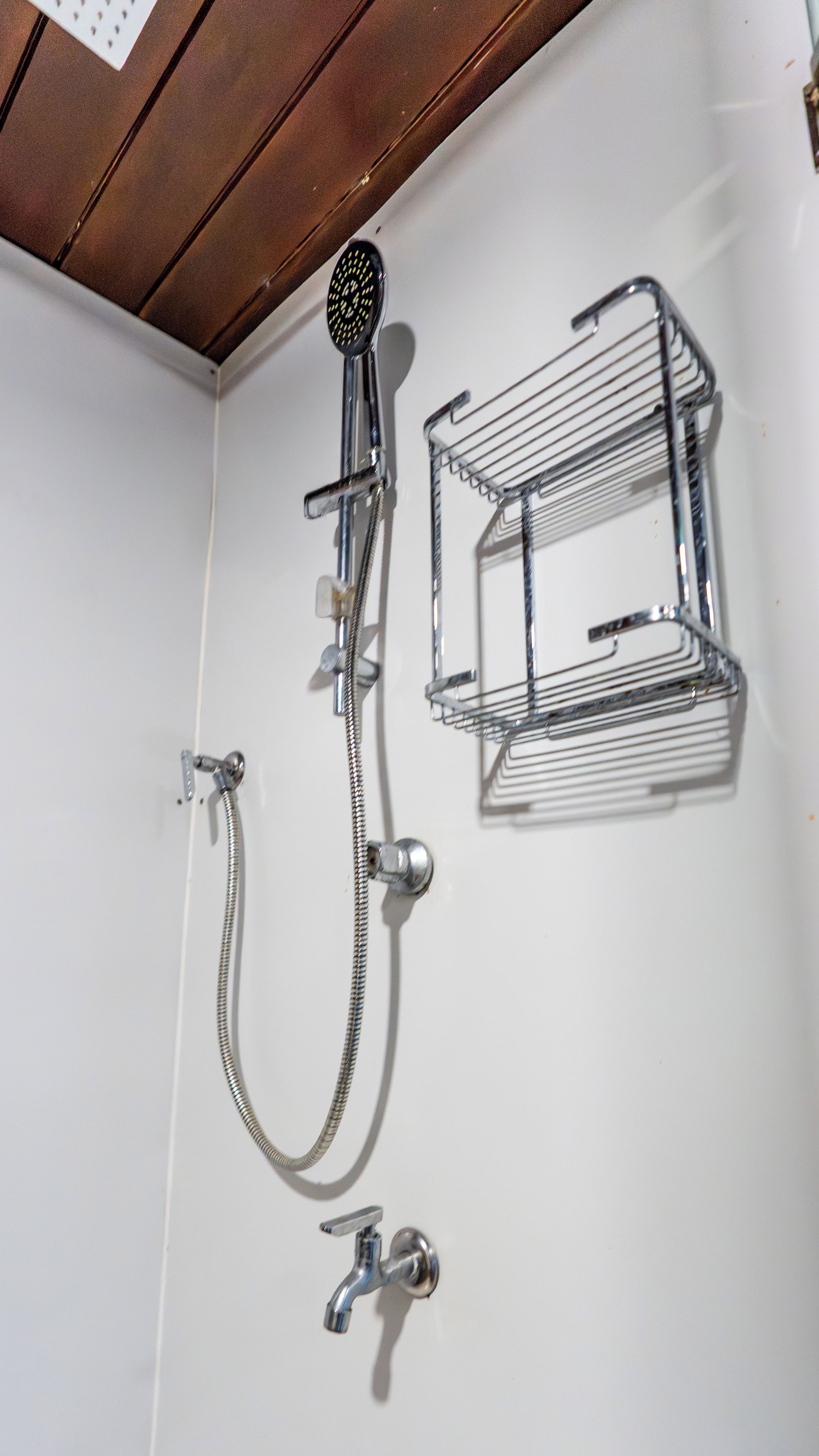 Een douche met een handdouche, een handdoekhouder aan de muur en een metalen plank.