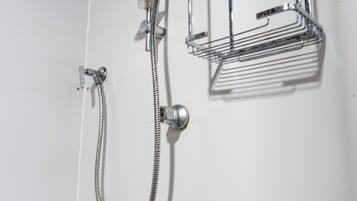 Een douche met een handdouche, een handdoekhouder aan de muur en een metalen plank.