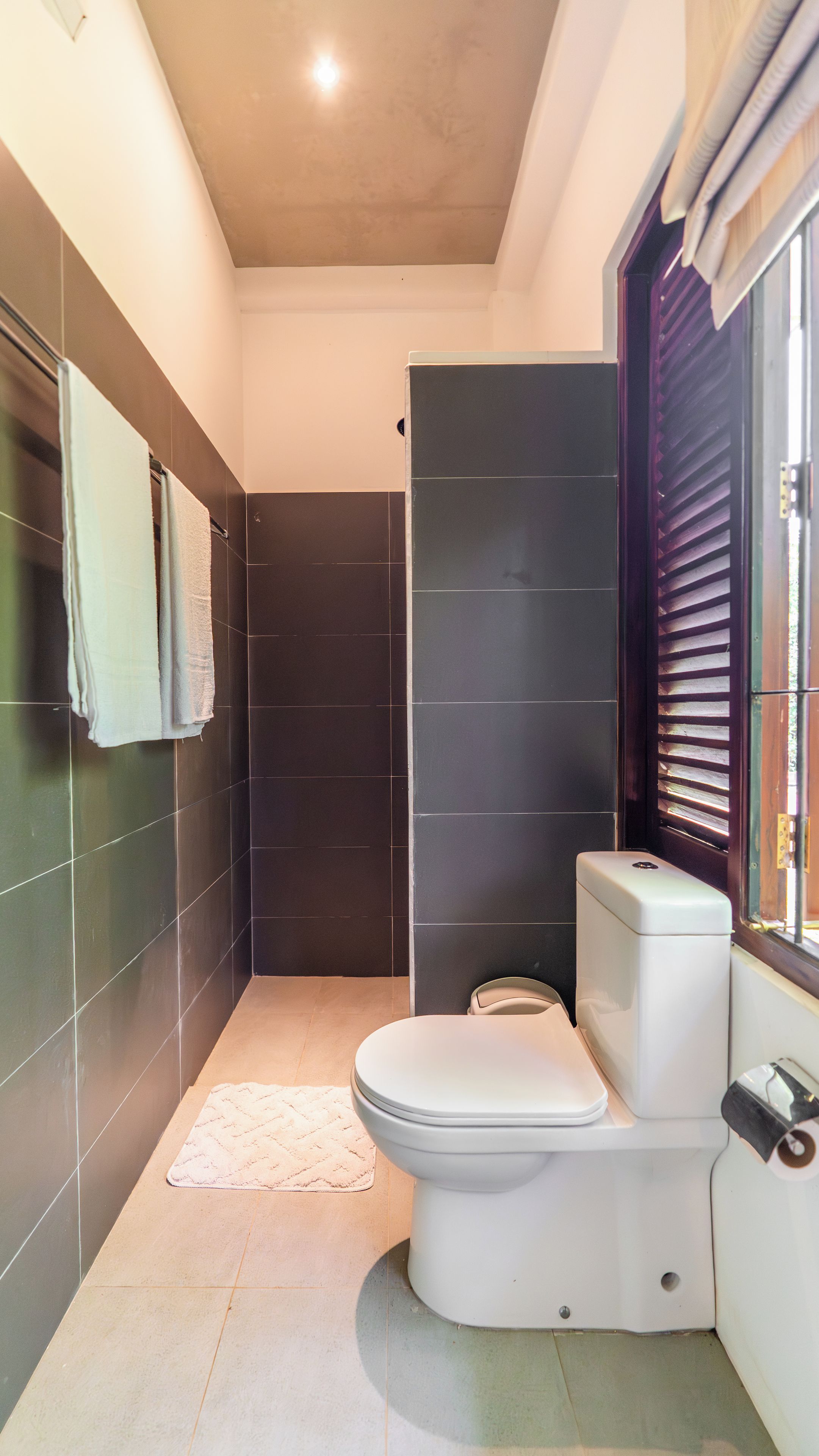 Une salle de bain moderne équipée de toilettes, d’une douche et d’une fenêtre avec des stores.
