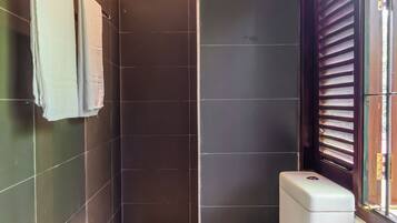 Une salle de bain moderne équipée de toilettes, d’une douche et d’une fenêtre avec des stores.
