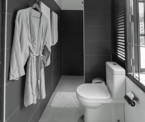 A modern bathroom with a toilet, a towel rack with robes, and a window with blinds.