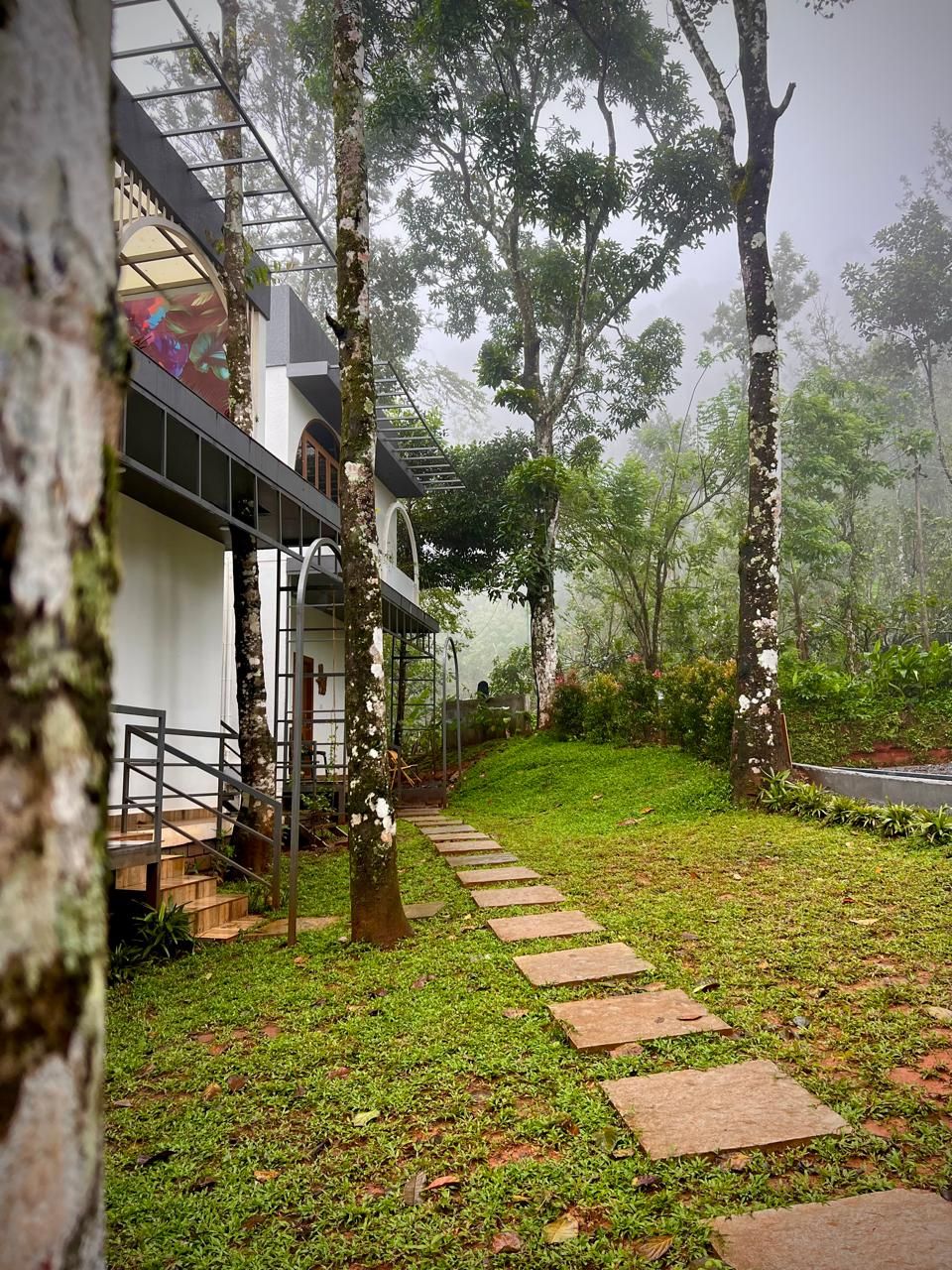 A pathway leading to a building with a modern design, surrounded by lush greenery and trees.