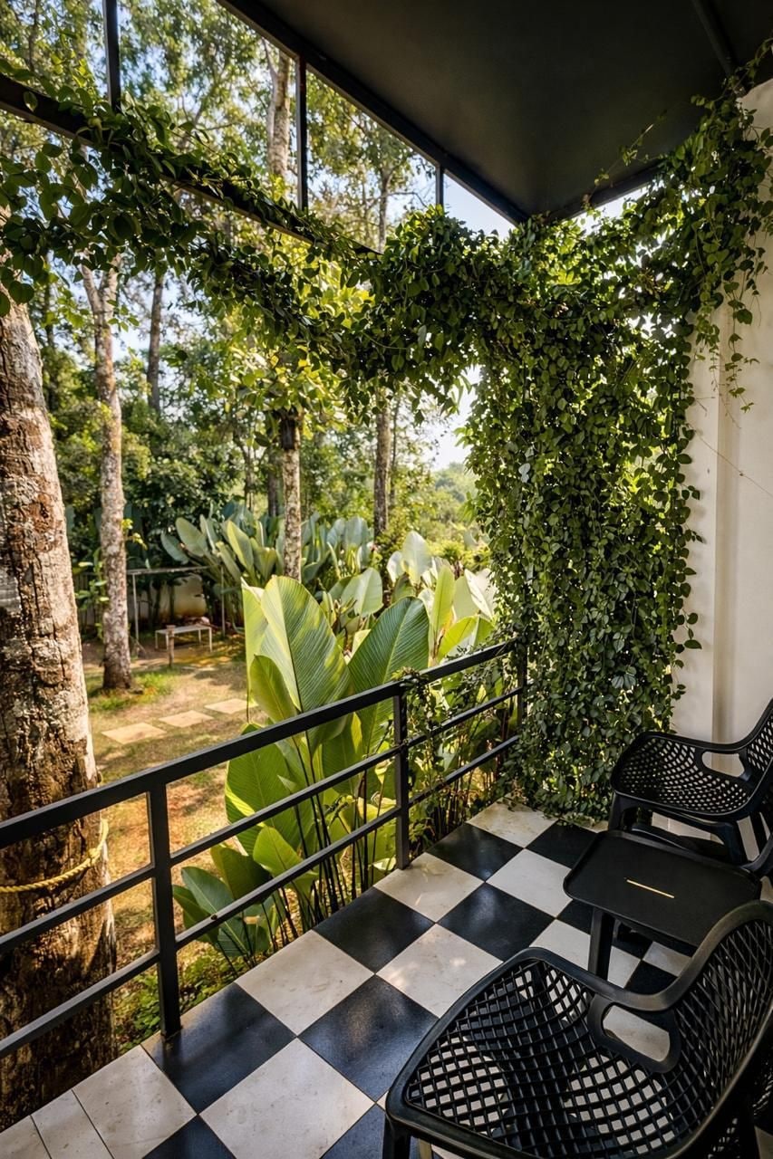 Un espacio al aire libre techado con piso a cuadros, sillas de metal negro y vista a un área boscosa.