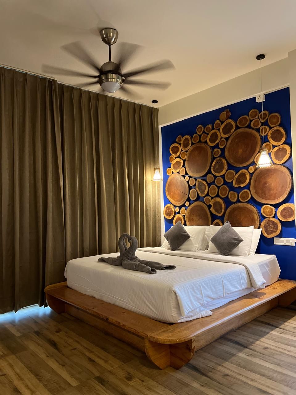 Un dormitorio con cama, cortinas, ventilador de techo y una pared con diseños circulares de madera.