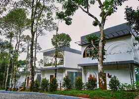 Un edificio moderno de varios pisos con techo plano, ventanas amplias y un jardín con árboles y arbustos.