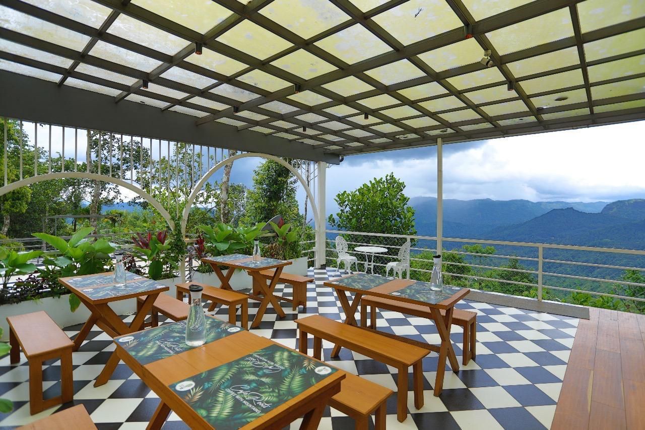 Un patio al aire libre con piso a cuadros, mesas y bancos de madera, y vistas a montañas.
