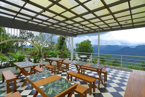 Une terrasse extérieure avec un sol à carreaux, des tables et des bancs en bois, et une vue sur les montagnes.