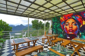An outdoor seating area with tables and chairs, a checkered floor, and a mural on the wall. - Roots Munnar (Anachal)