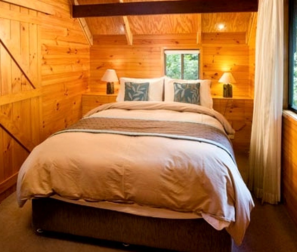 A wooden cabin bedroom with a bed, two bedside tables, lamps, and a window.