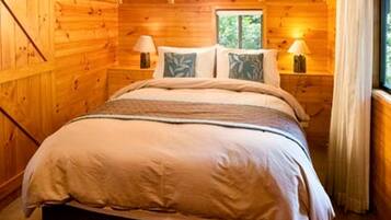 A wooden cabin bedroom with a bed, two bedside tables, lamps, and a window.