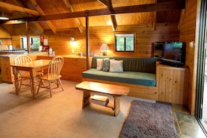A cozy cabin interior with a dining area, a sofa, a television, and a window.