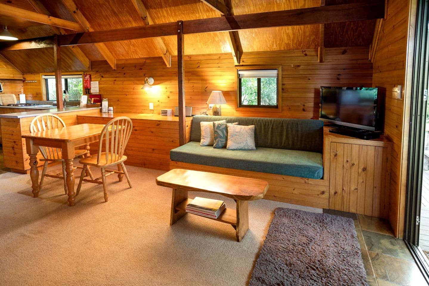 A cozy cabin interior with a dining area, a sofa, a television, and a window.