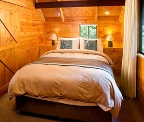 A wooden cabin bedroom with a bed, two bedside tables, lamps, and a window.