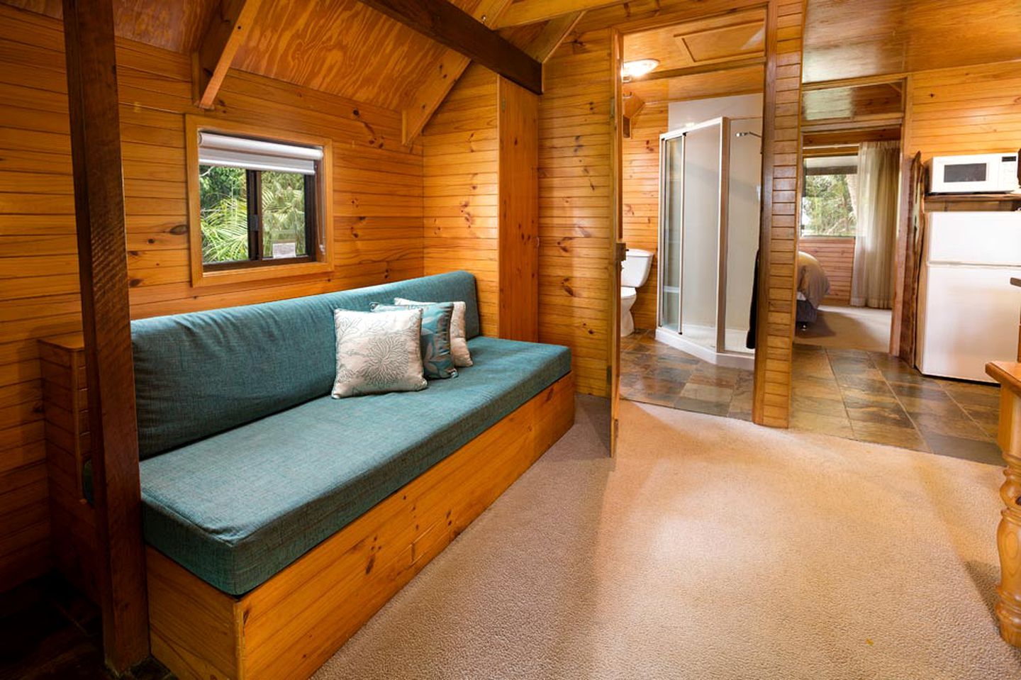 L’intérieur d’un chalet en bois comprend un canapé, une fenêtre, une douche et un coin cuisine.