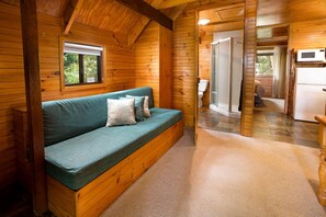 A wooden cabin interior with a sofa, a window, a shower, and a kitchen area. - Idyllic Forest Cabin Perfect for a Hiking Trip near D'aguilar National Park, Queensland (Mount Glorious)