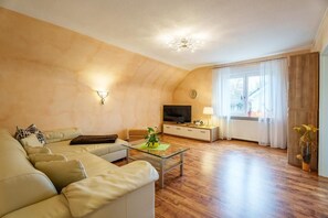 Una sala de estar con un sofá, una mesa de centro de vidrio, un televisor y una ventana con cortinas.