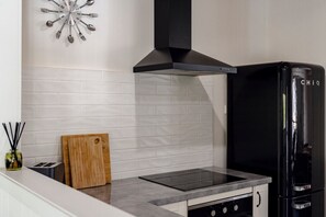 A kitchen with a black range hood, a black refrigerator, and a wooden cutting board on the counter.