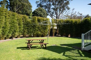 Quintal gramado com mesa de piquenique e uma estrutura de metal.