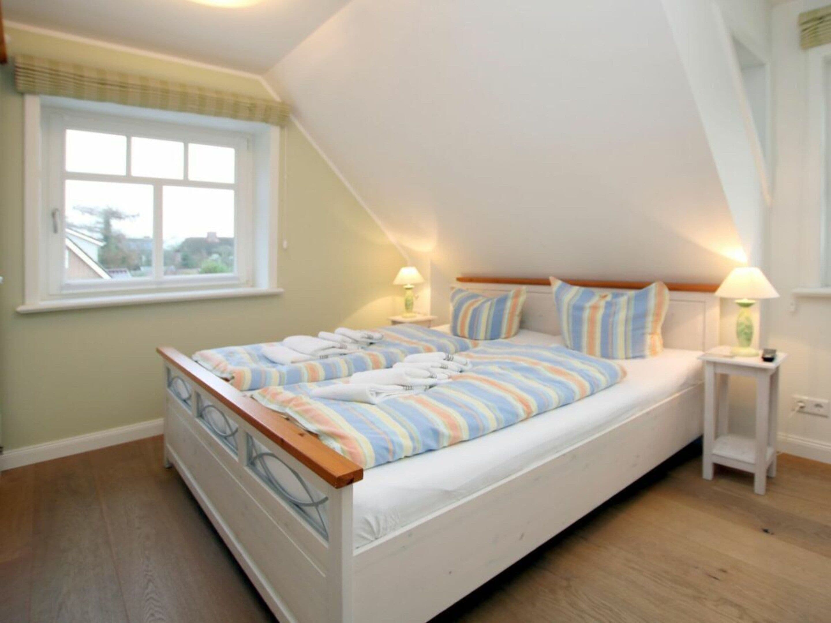 Een slaapkamer met een enkel bed, twee nachtkastjes, een raam en een schuine plafond.