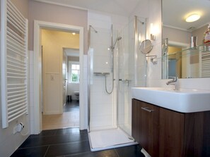 Ein modernes Badezimmer mit Duschkabine aus Glas, einem weißen Waschbecken und einem Holz-Waschtisch.